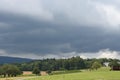 Heavy, thick, thunder, stormy, rainy clouds over the mixed forest and meadows with harvested field