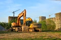 Heavy tracked excavator at a construction site on a background of a residential building and construction cranes on a sunny day Royalty Free Stock Photo