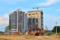 Heavy tracked excavator at a construction site on a background of a residential building and construction cranes on a sunny day