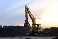 Heavy tracked excavator at a construction site on a background sunset.