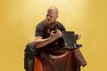 Comic portrait of muscular bearded bald man, blacksmith in leather apron or uniform isolated on yellow studio background