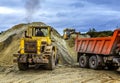 Heavy wheel excavator machine working at sunset, loads the sand into the truck Royalty Free Stock Photo