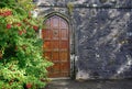 Heavy wooden door set in a dark stone wall with flowers beside