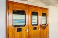 Cruise ship heavy varnished wood exterior doors with windows reflecting the sea.