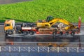 Heavy yellow excavator on transportation truck with long trailer platform on the highway wet asphalt after rain in the city