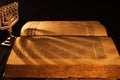 Hebrew Bible in candle light on dark background. Shadow from menorah on open pages of Jewish prayer book in the dark