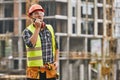 Hecking work. Professional young builder in working uniform and red protective helmet talking to crane operator by