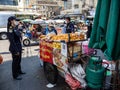 Bustling street market with a food vendor and a lady in blue uniform and a tuk-tuk in the background in Bangkok, Thailand