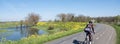 floodplanes of river waal and woman with bike on dyke in the netherlands under blue spring sky with yellow flowers