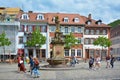Square called `Kornmarkt` in old city center with fountain with golden Madonna statue and people walking by on sunny day