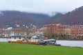 Boat permanently anchored at the Neckar river meadow near city center of Heidelberg, with old buildings and beautiful hill landsca