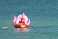 Hel, Poland - 08.01.2021: Beach lifeguard rowing in his orange boat carrying a big pink inflatable flamingo back to the Royalty Free Stock Photo