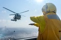 Helicopter deck officer give hand signal to Sikorsky S-70 Sea Hawk helicopter hovering above helicopter deck of Navy ship to