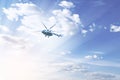 A helicopter flies high in the blue sky, in the rays of the sun and clouds. Rescue operation. Military equipment transport