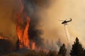 helicopter flying over wildfire, dropping water to extinguish flames