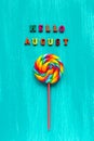 Hello August text from colorful letters and spiral multi-colored round lollipop on stick on wooden blue background