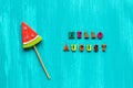 Hello August text from colorful letters and watermelon lollipop on stick on wooden blue background. Concept Creative Top