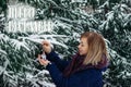 Hello, December. Outdoor winter Christmas portrait of Woman in snowy forest. Smiling Caucasian blonde woman decorates fir tree for Royalty Free Stock Photo