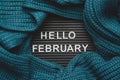 Hello February text on a letter board with a knitted green-blue, warm, cozy scarf. Winter concept