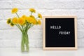 Hello Friday words on black letter board and bouquet of yellow dandelions flowers on table against white brick wall. Concept Happy