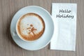 Hello Holiday text on paper with hot cappuccino coffee cup on table background at the morning