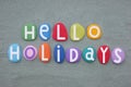 Hello Holidays, creative slogan composed with stone letters over green sand Royalty Free Stock Photo