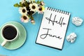 Hello June concept on notebook with crash papers and roses flowers and cup of coffee isolated on blue