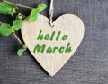 Hello March greeting card with decorative heart and green spring tree branch on old wooden background.Springtime concept.