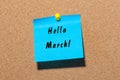 Hello March - handwriting on a blue paper pinned at cork noticeboard. Beginning of spring concept