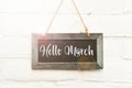 Hello March handwritten text on hanging sign board againt white outdoor wall