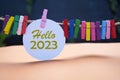 Hello 2023. New Year 2023 concept with golden text on white circle paper and colorful wooden clips on rope.