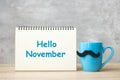 Hello November with paper notepad, Blue coffee cup or tea mug and Black mustache decor on table. International Men day, Happy Royalty Free Stock Photo