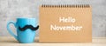 Hello November with paper notepad, Blue coffee cup or tea mug and Black mustache decor on table. International Men day, Happy Royalty Free Stock Photo