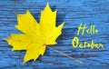 Hello October.Golden autumn maple leaf on a blue colored vintage wooden texture.Autumnal background with text. Royalty Free Stock Photo