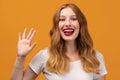 Portrait of friendly woman with wavy redhead, standing waving hand, looking at camera with engaging toothy smile Royalty Free Stock Photo