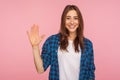 Hello! Portrait of cheerful friendly hospitable girl in checkered shirt standing with raised palm gesturing hi