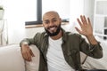 Hello. Portrait of happy mature latin man waving hand and smiling to camera, sitting on sofa at home Royalty Free Stock Photo