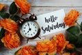 Hello Saturday card and alarm clock with orange flower decoration on wooden background Royalty Free Stock Photo