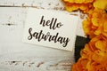 Hello Saturday Card with Blooming flower on wooden background