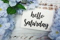 Hello Saturday Card with Blooming flower on wooden background