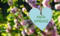 Hello Spring greeting card with decorative white wooden heart with text on a blurred pink sakura blossom background. Royalty Free Stock Photo