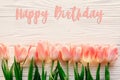 happy birthday text sign on pink tulips on white rustic wooden background flat lay. spring top view of flowers in soft morning li Royalty Free Stock Photo