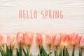 hello spring text sign, beautiful pink tulips on white rustic wooden background flat lay. flowers in soft morning sunlight with s Royalty Free Stock Photo