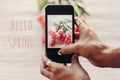 Hello spring text sign, hand holding phone taking photo of styli