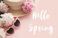 Hello Spring text sign on stylish girly pink retro sunglasses, white and pink peonies, straw hat on pastel pink paper, flat lay.