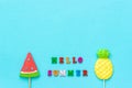 Hello summer colorful text, pineapple and watermelon lollipops on stick on blue paper background. Concept vacation or holidays