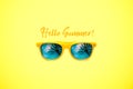 Hello Summer concept image: yellow sunglasses with palm tree reflections isolated in large yellow background.