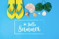 Hello Summer text on blue background, Yellow sandals with green tropical palm leaf and shell