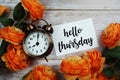 Hello Thursday card and alarm clock with orange flower decoration on wooden background Royalty Free Stock Photo