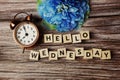 Hello Wednesday alphabet letters with alarm clock and blue flower on wooden background